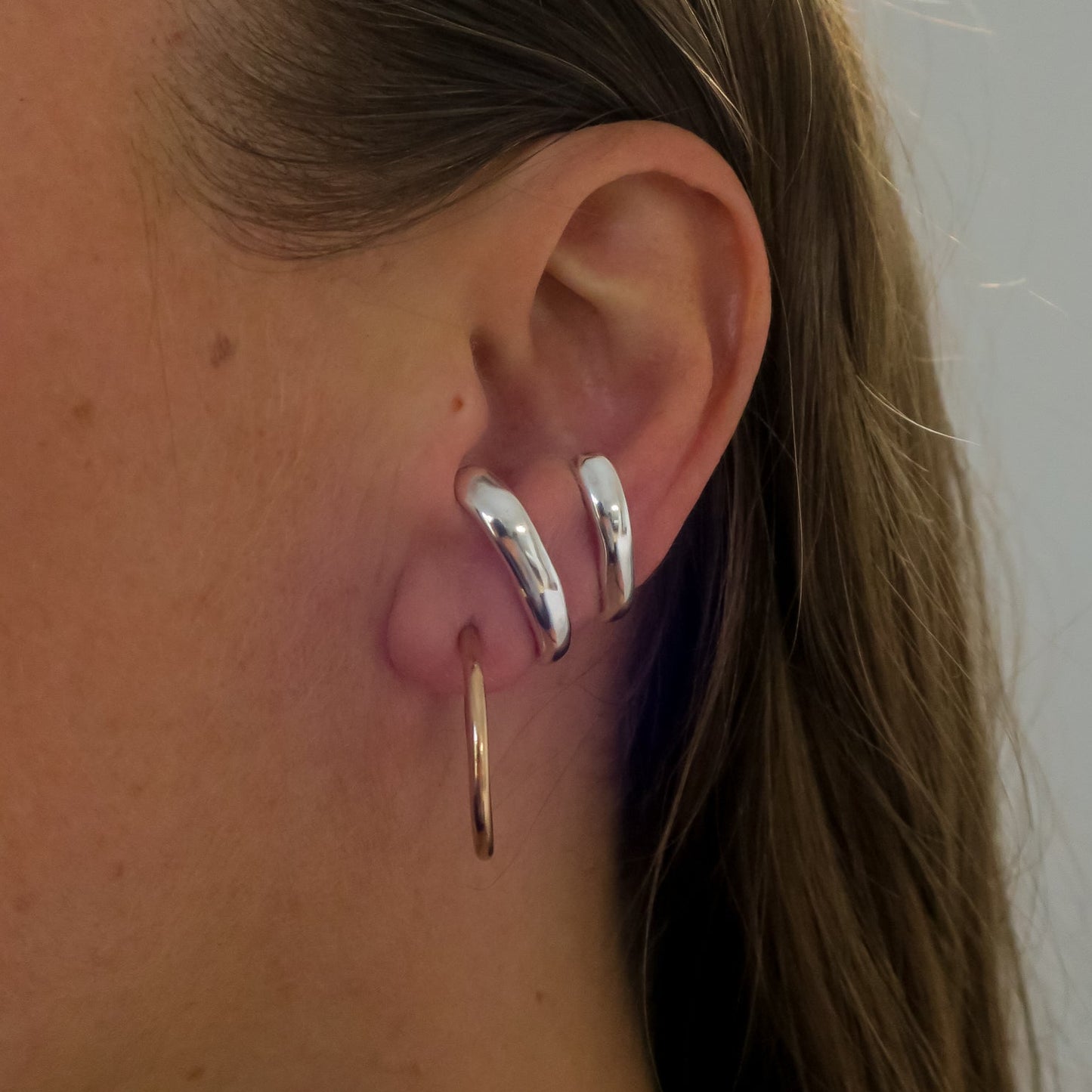 Close-up of a person's ear with multiple earrings against a neutral background