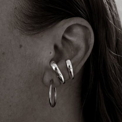 Close-up of an ear wearing silver hoop earrings and a cuff.