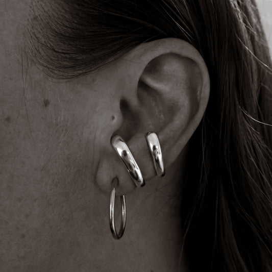 Close-up of an ear wearing silver hoop earrings and a cuff.