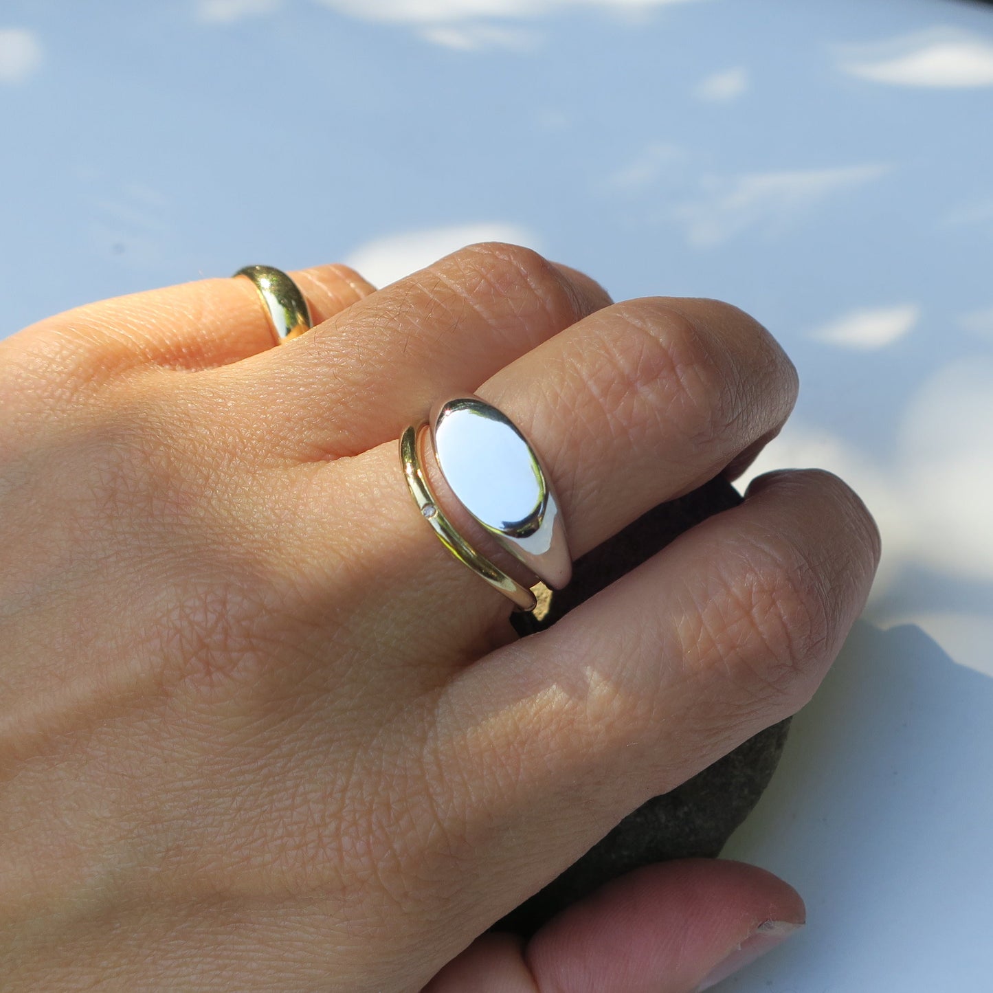 Hand wearing a gold ring on a white surface with shadows