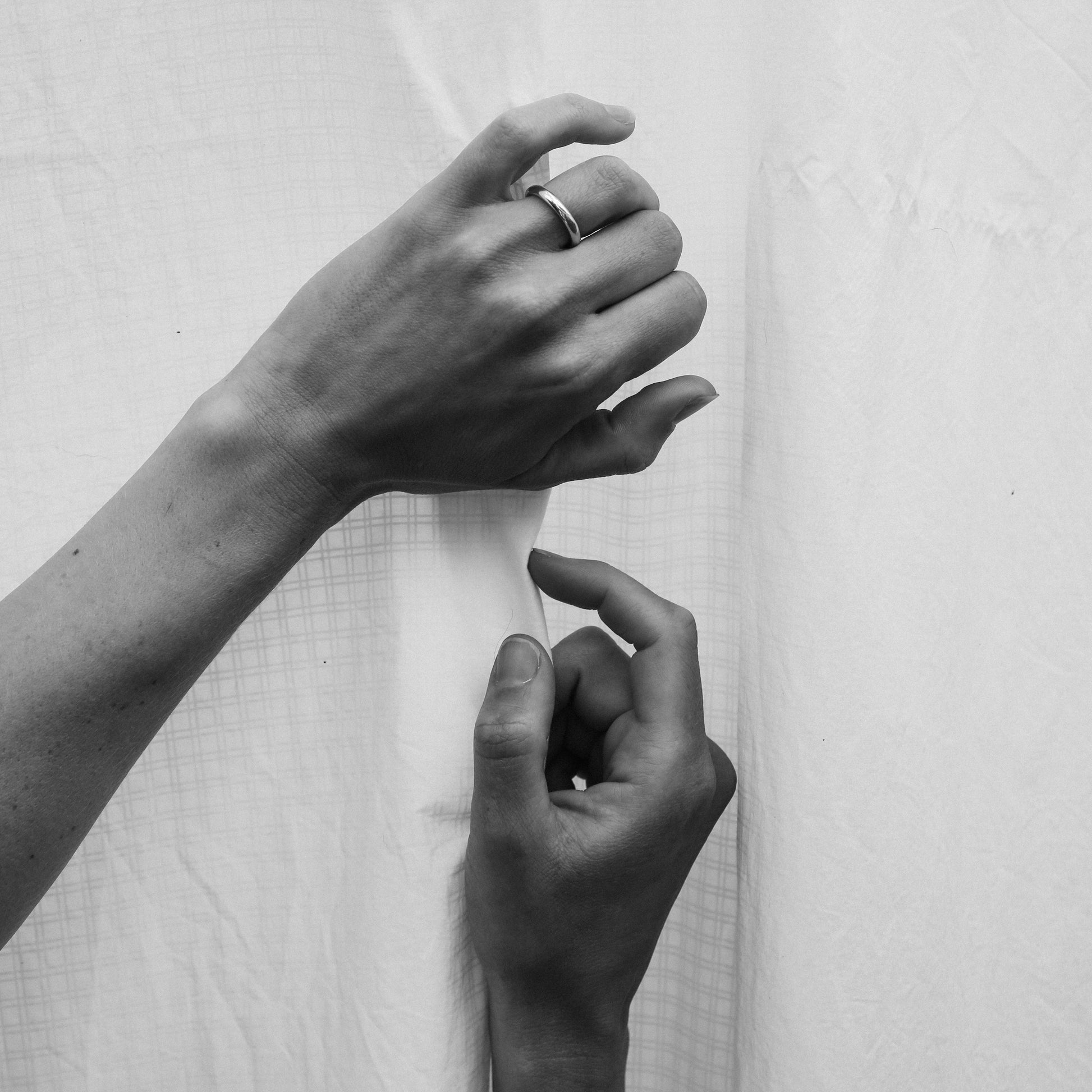 a black and white image of two hands on a white fabric backdrop with a gold band.
