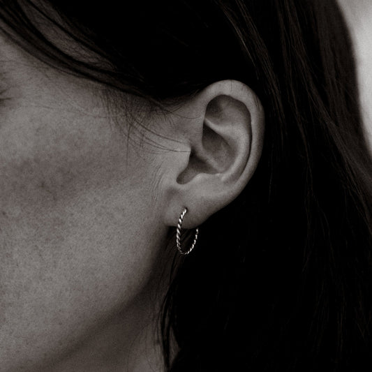Close-up of an ear wearing a silver hoop earring with dark hair.