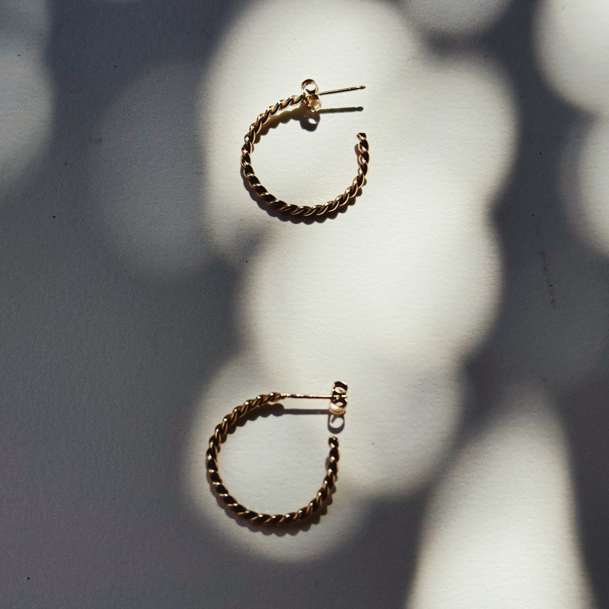 fine twisted gold hoop earrings on a white and shadowy background