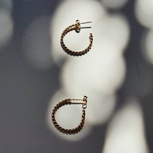 fine twisted gold hoop earrings on a white and shadowy background