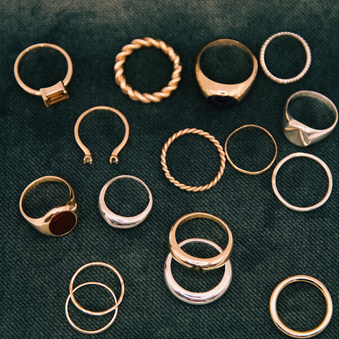 Collection of gold and silver rings on a dark green fabric background