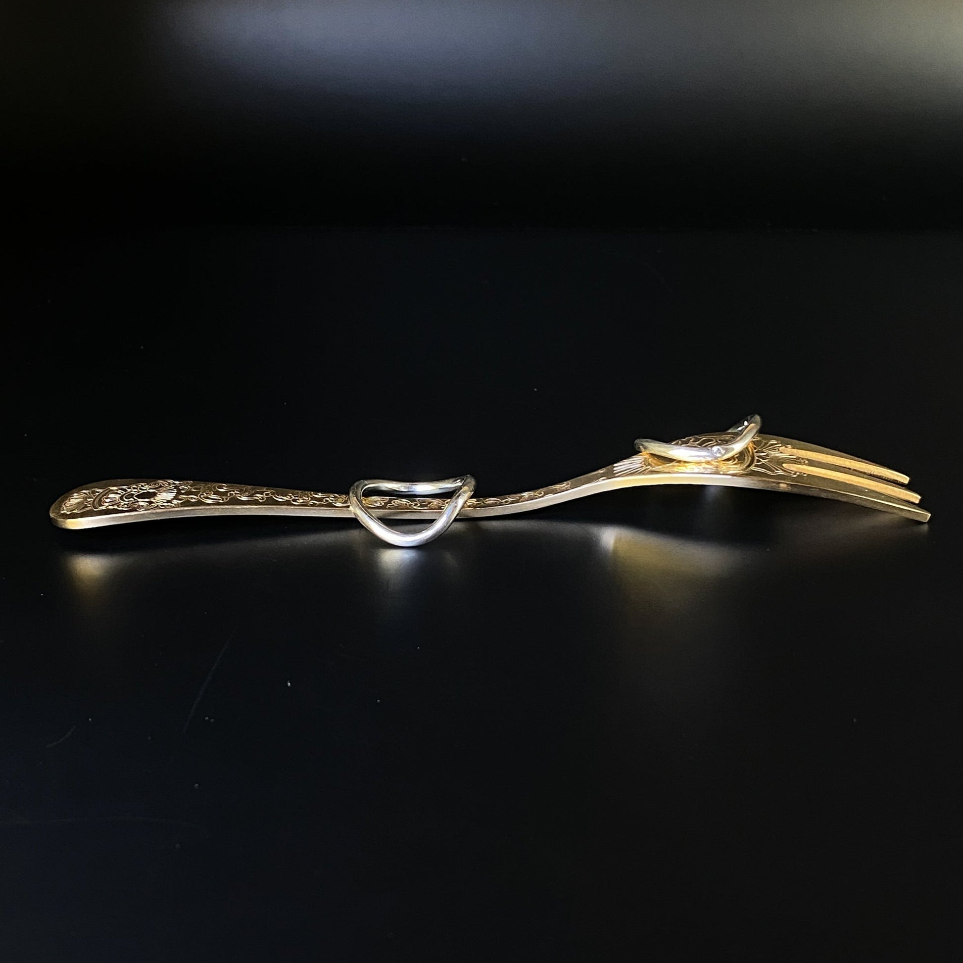 Gold fork on a black background featuring two sculptural rings that are fine and have gentle curves
