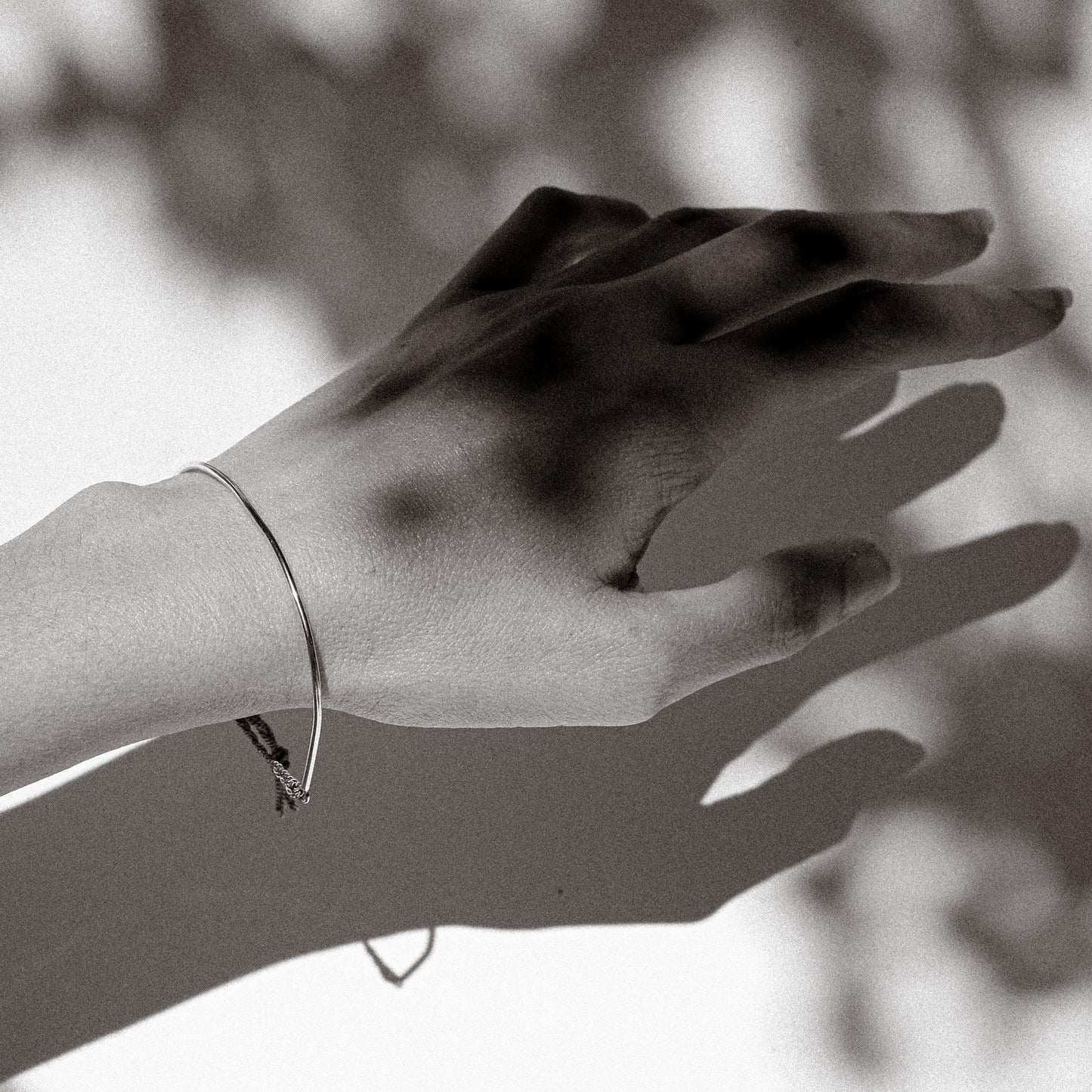 Black and white photo of a hand with a bracelet against a blurred background
