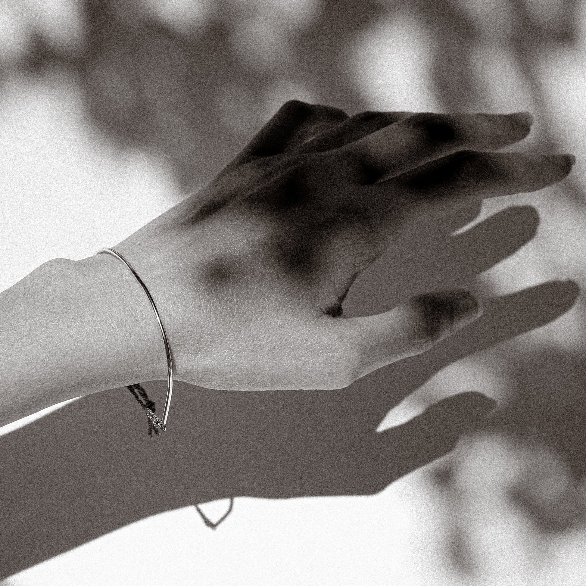 Black and white photo of a hand with a bracelet against a blurred background