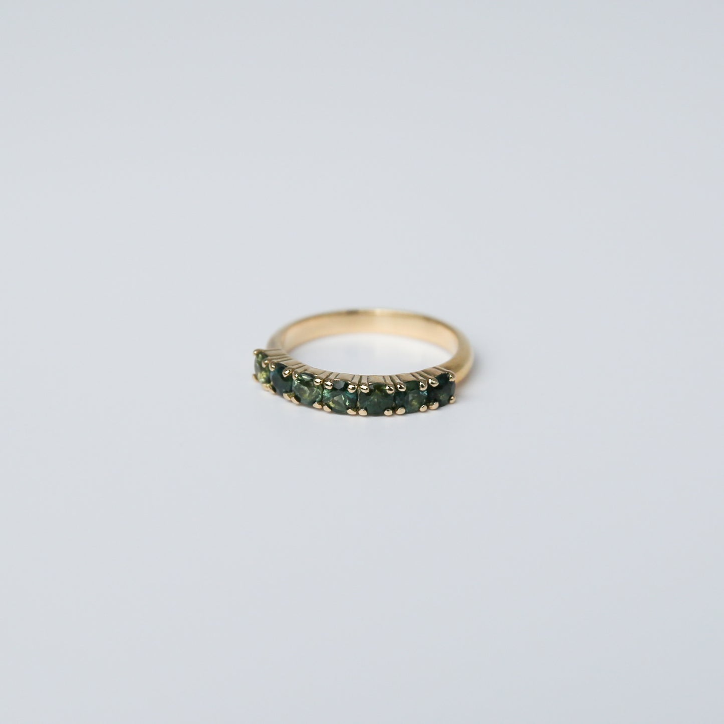 Gold ring with green gemstones on a light gray background