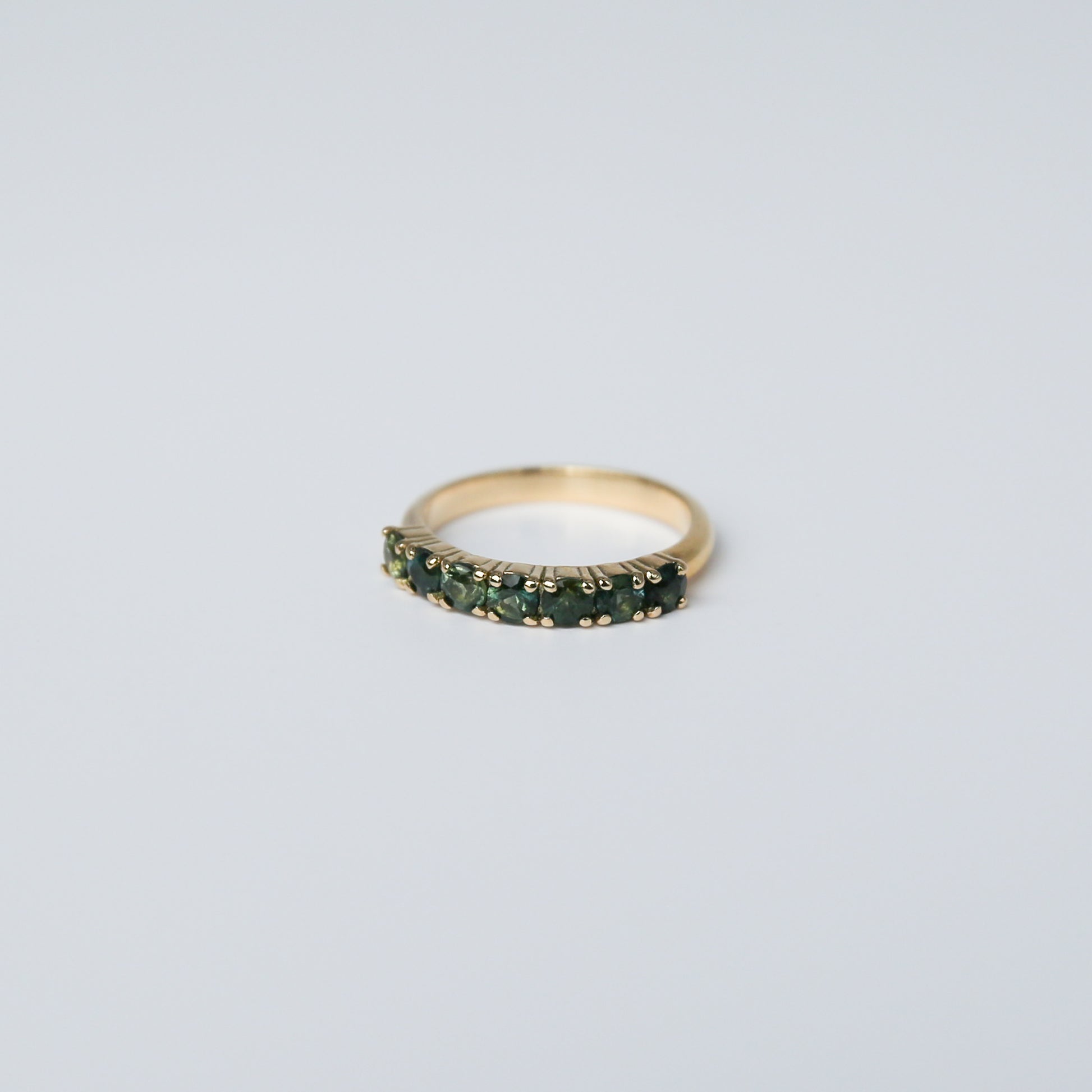 Gold ring with green gemstones on a light gray background