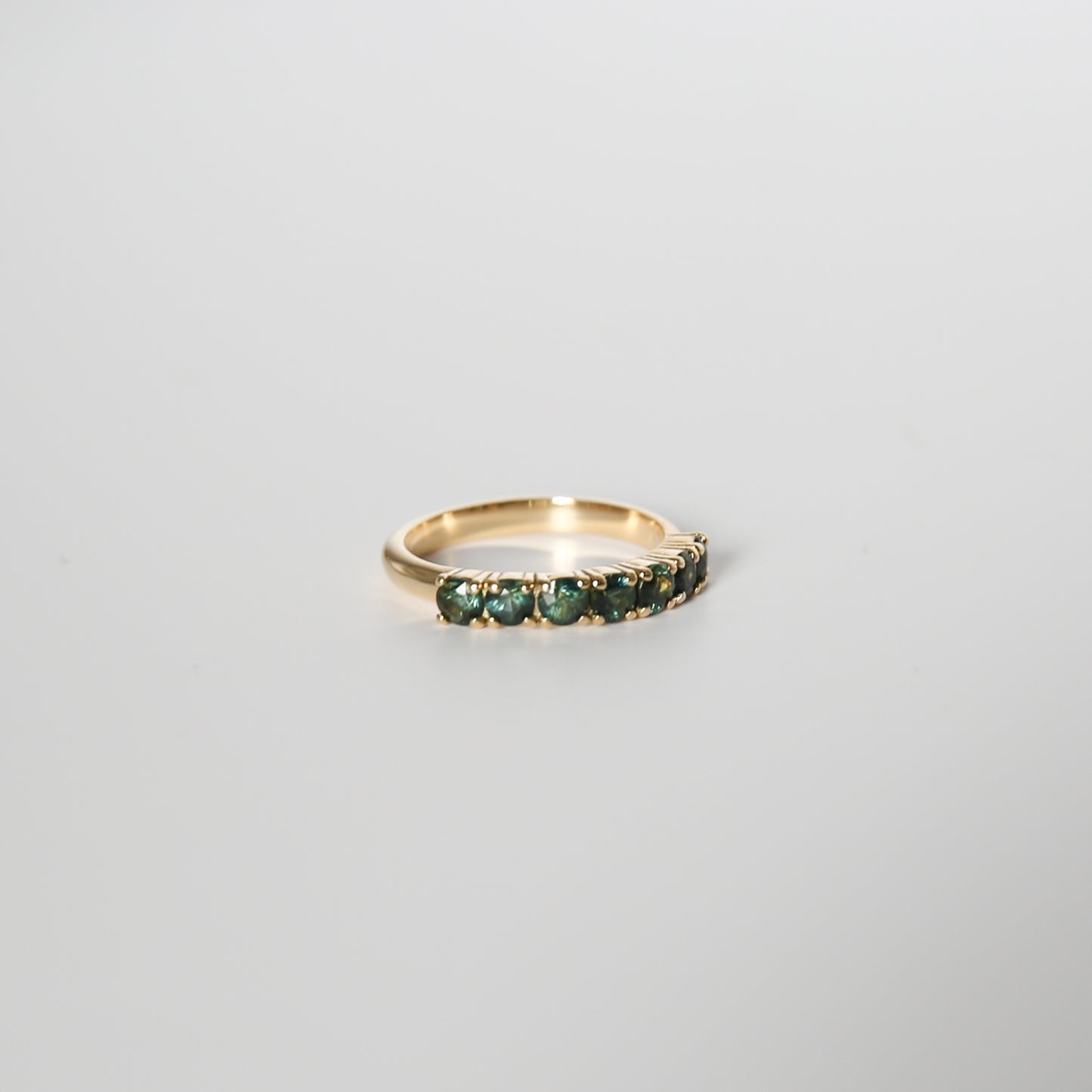 Gold ring with green gemstones on a light gray background