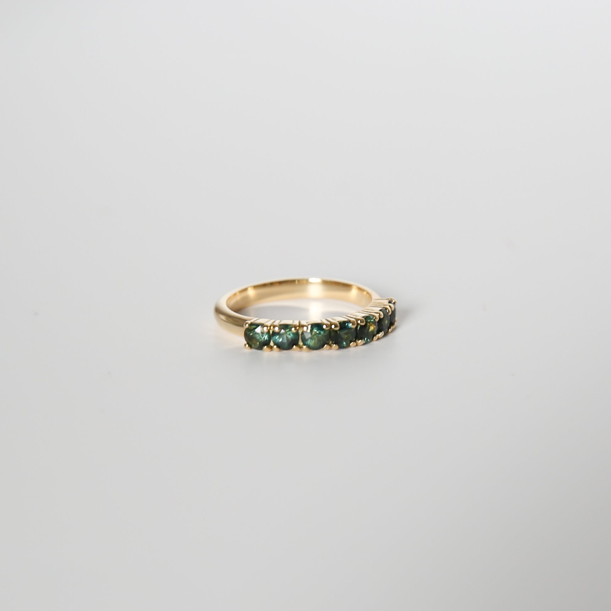 Gold ring with green gemstones on a light gray background