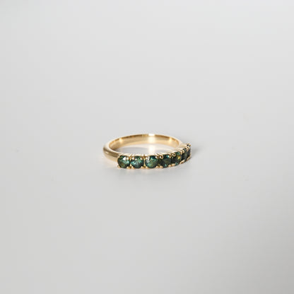 Gold ring with green gemstones on a light gray background