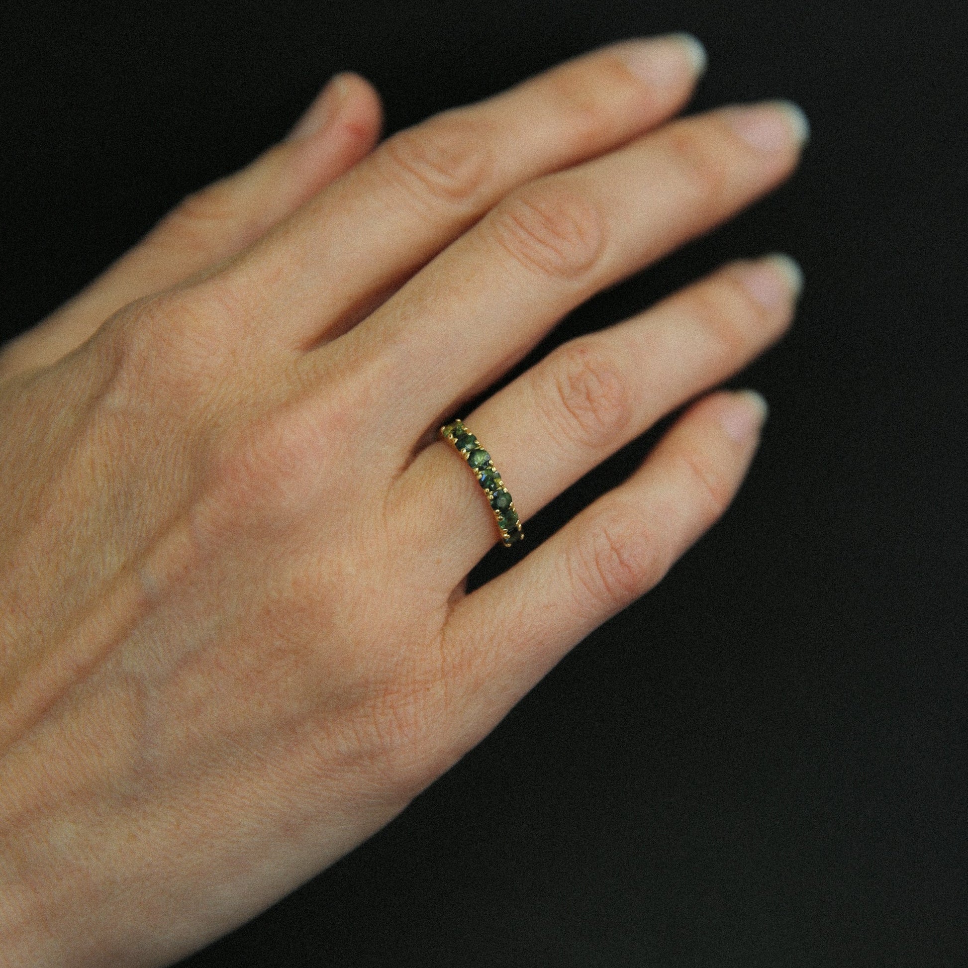 Hand wearing a ring with green gemstones against a black background