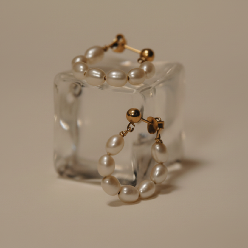 Pearl and gold earrings on a clear stand against a beige background