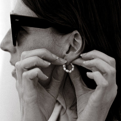 Person wearing sunglasses and adjusting an earring with a plain background