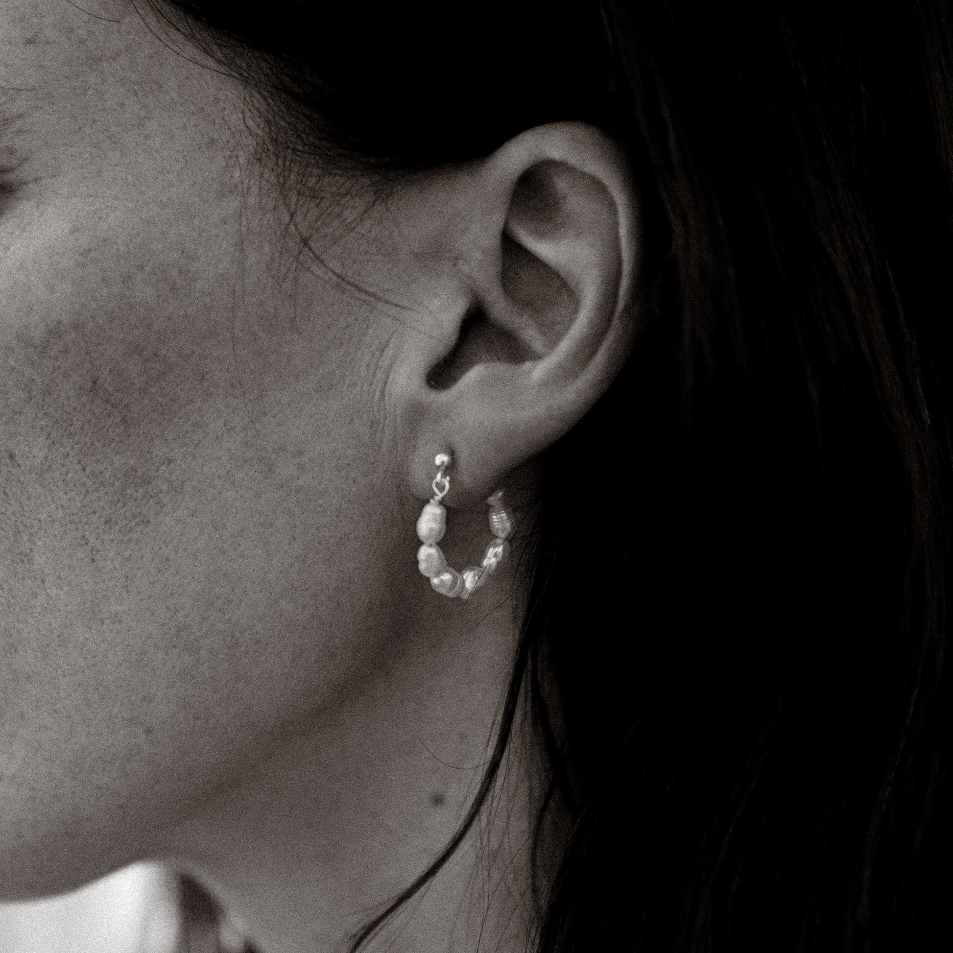 Close-up of an ear wearing a small hoop earring with pearls.