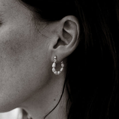Close-up of an ear wearing a small hoop earring with pearls.