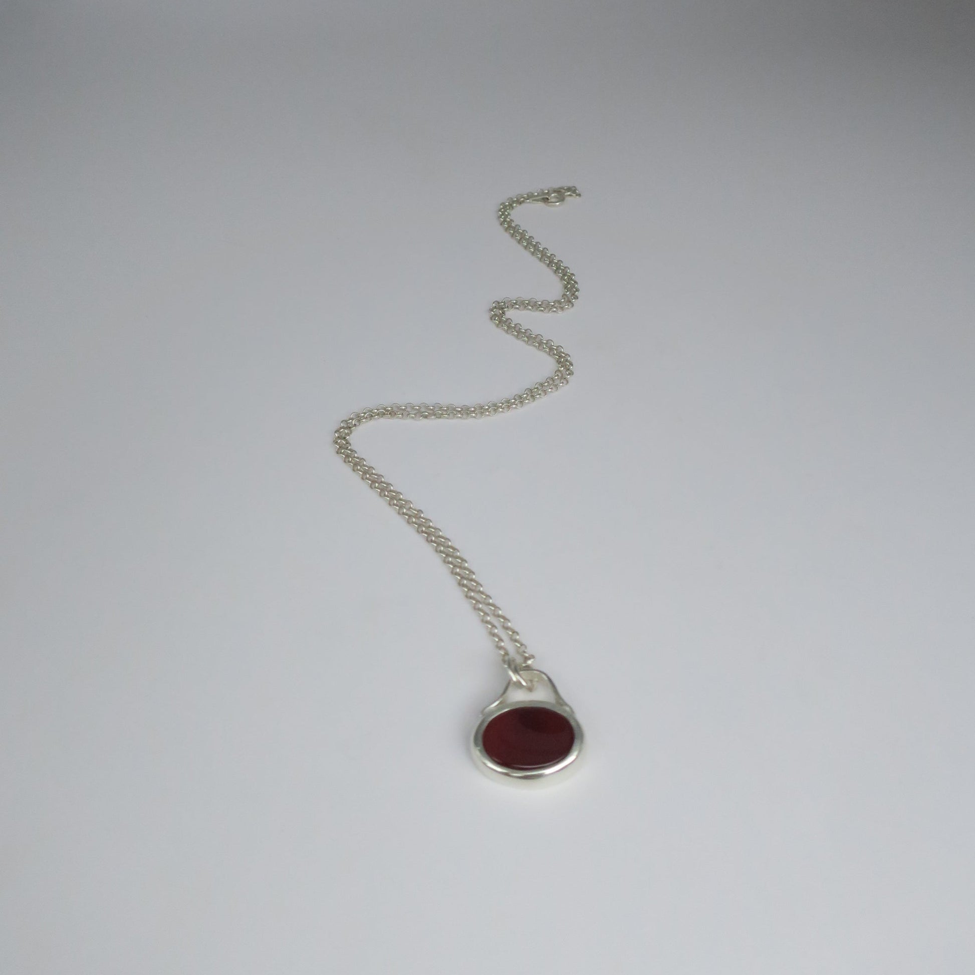 Silver necklace with a red stone pendant on a white background
