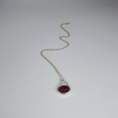 Silver necklace with a red stone pendant on a white background