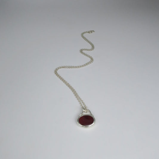 Silver necklace with a red stone pendant on a white background