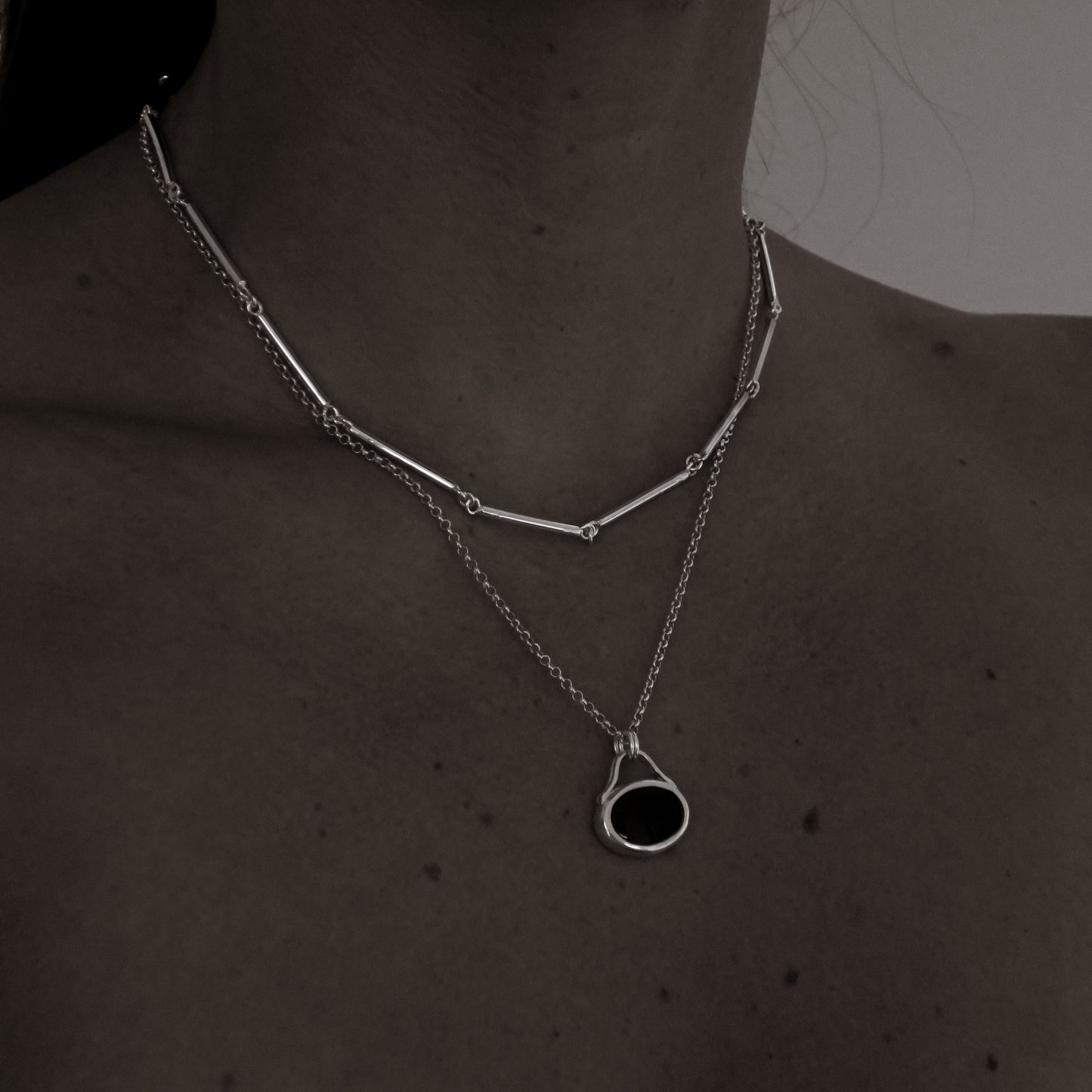 Silver necklace with a black pendant on a person's neck against a dark background