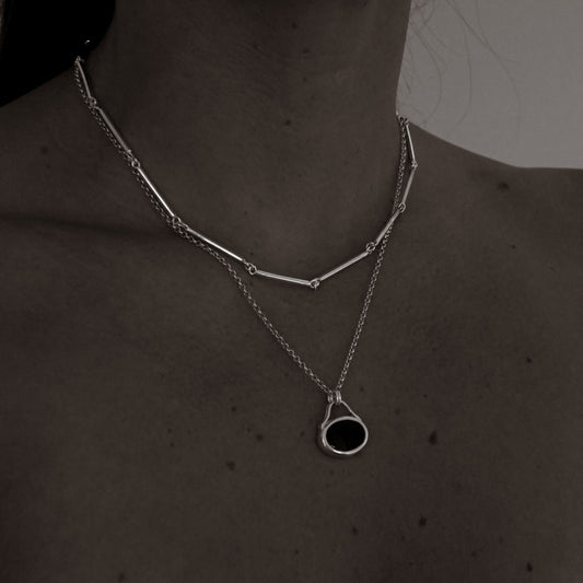 Silver necklace with a black pendant on a person's neck against a dark background