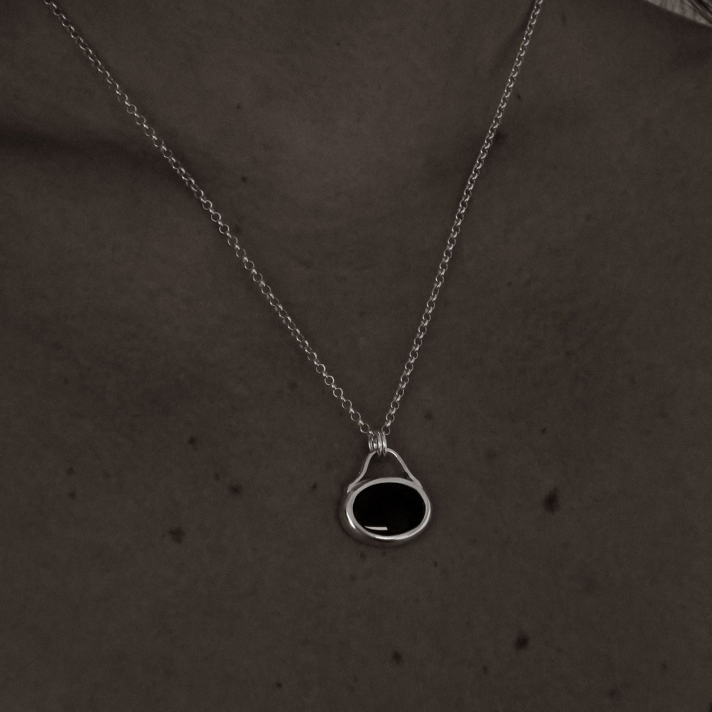 Silver necklace with a black pendant on a person's neck against a dark background