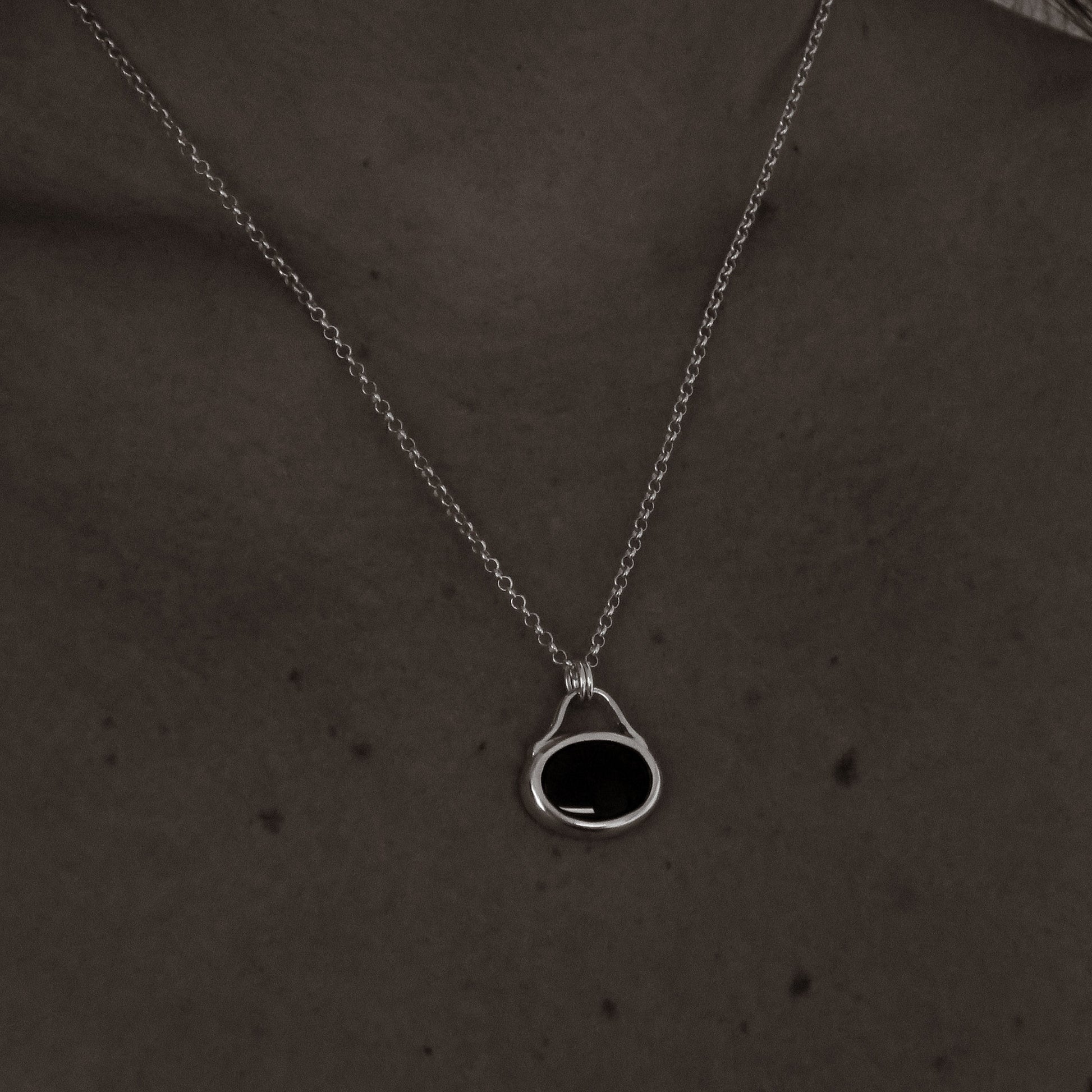 Silver necklace with a black pendant on a person's neck against a dark background