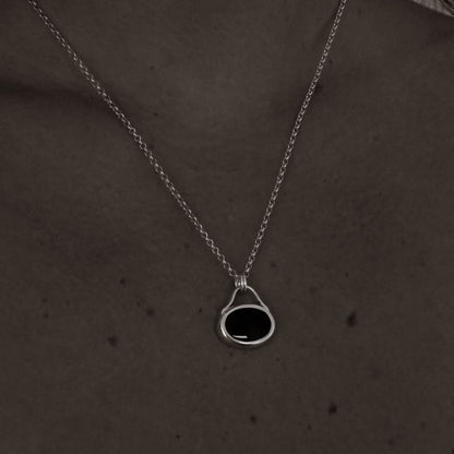 Silver necklace with a black pendant on a person's neck against a dark background