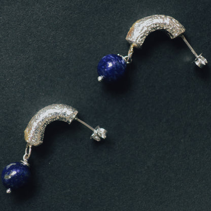 Pair of silver earrings with blue beads on a dark background