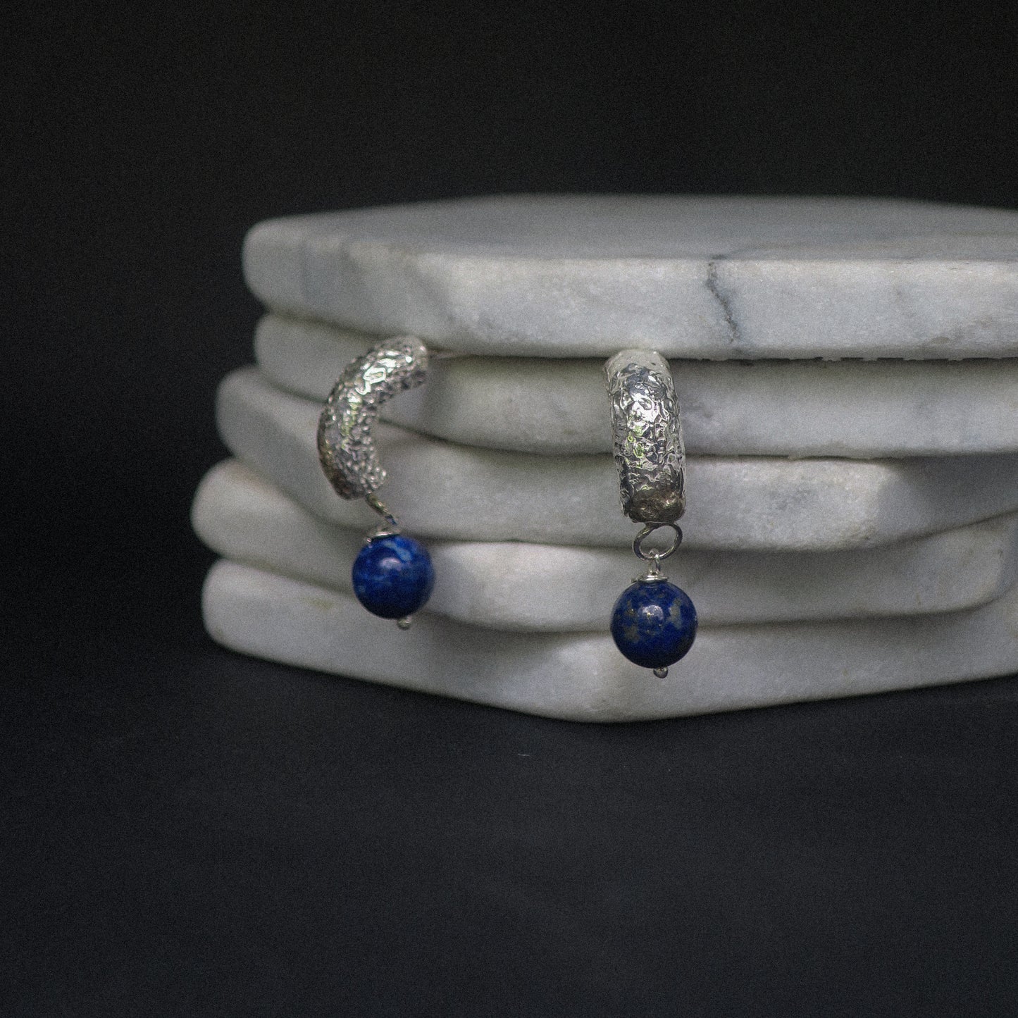 Silver hoop earrings with blue beads on a marble surface