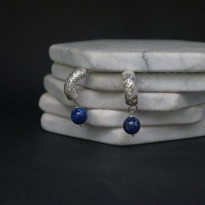 Silver hoop earrings with blue beads on a marble surface