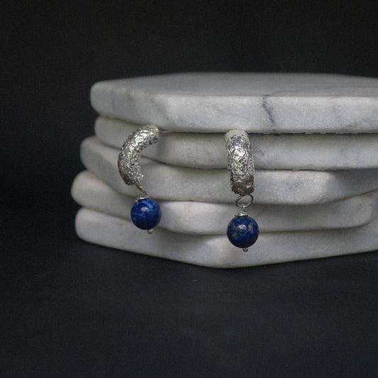 Silver hoop earrings with blue beads on a marble surface