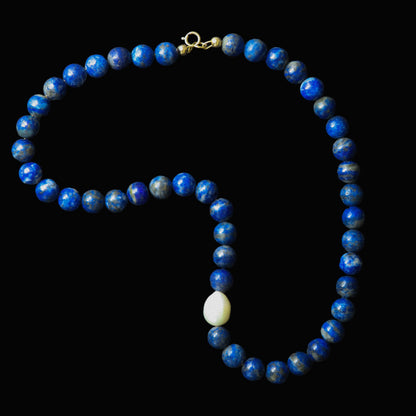 Blue beaded necklace with a white pearl on a dark background