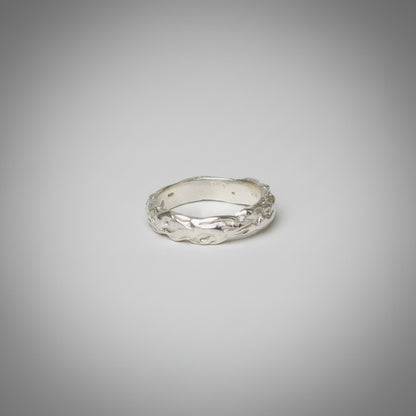 Silver ring with a textured design on a grey background
