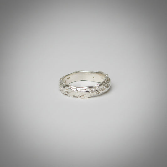 Silver ring with a textured design on a grey background