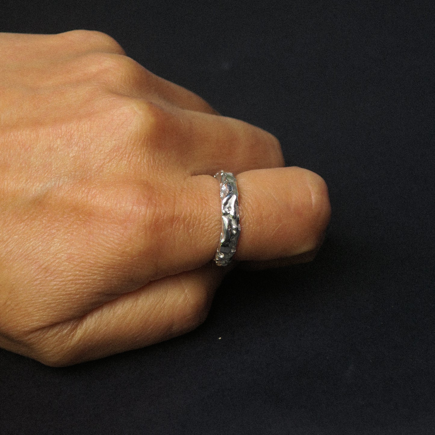Silver ring on a finger against a black background