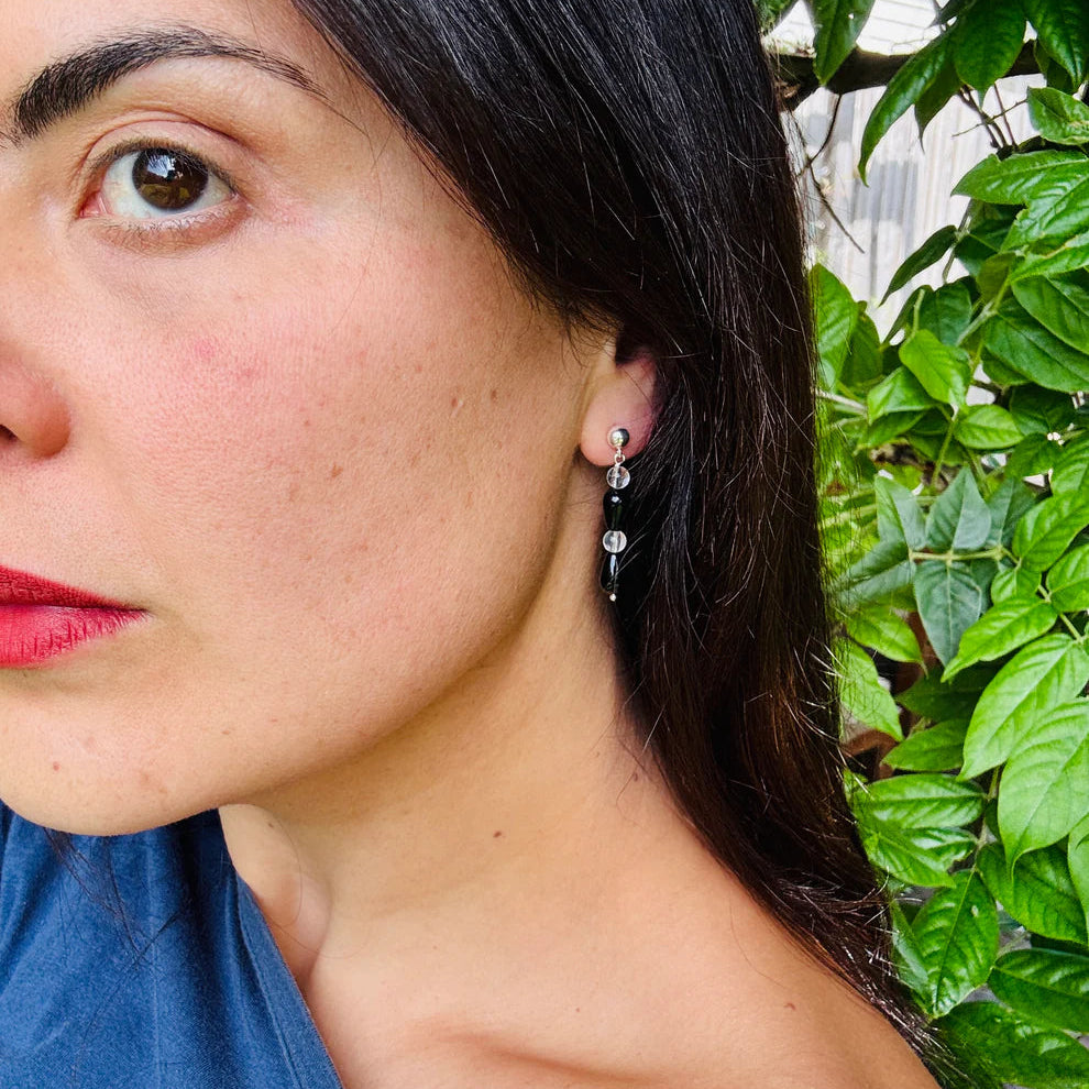 Close-up of a woman's face with earrings, wearing a blue top, against a green leafy background