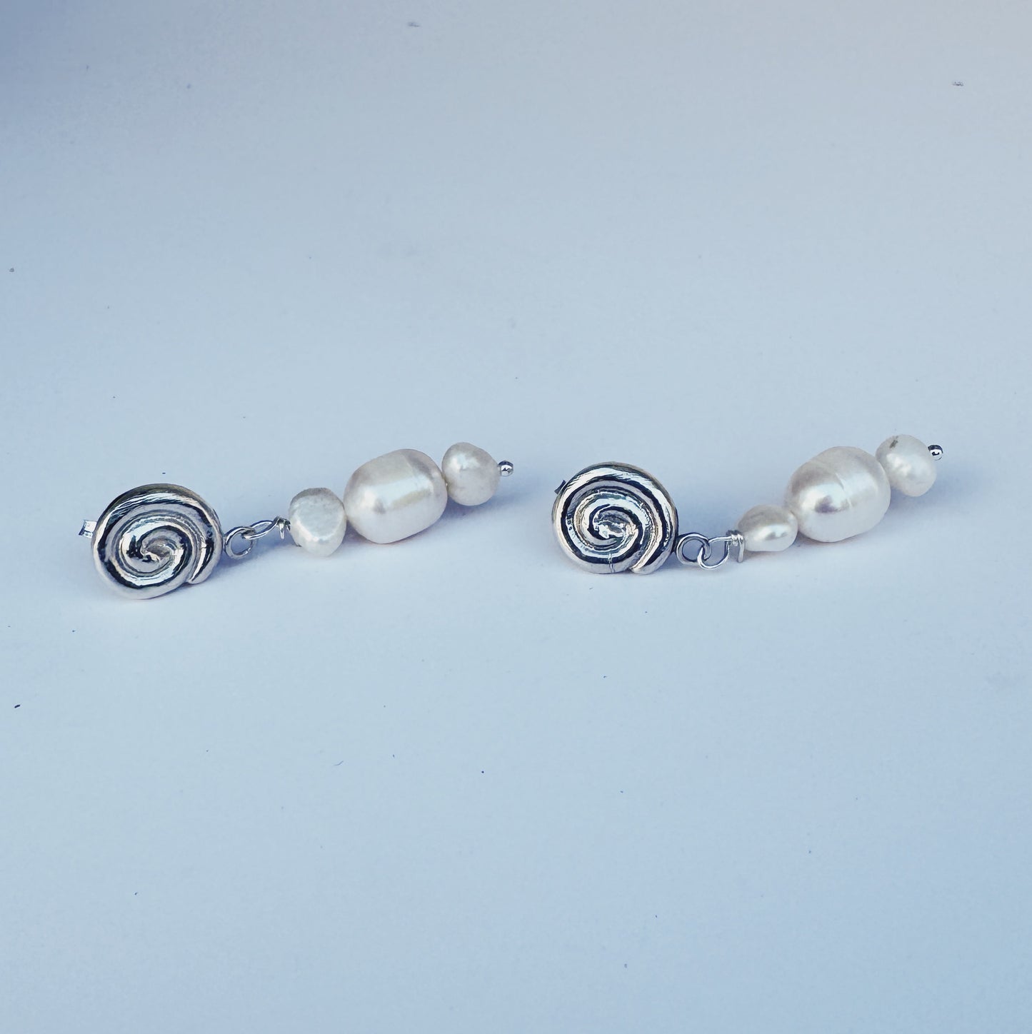 Pair of earrings with pearl beads and silver spiral designs on a light blue background