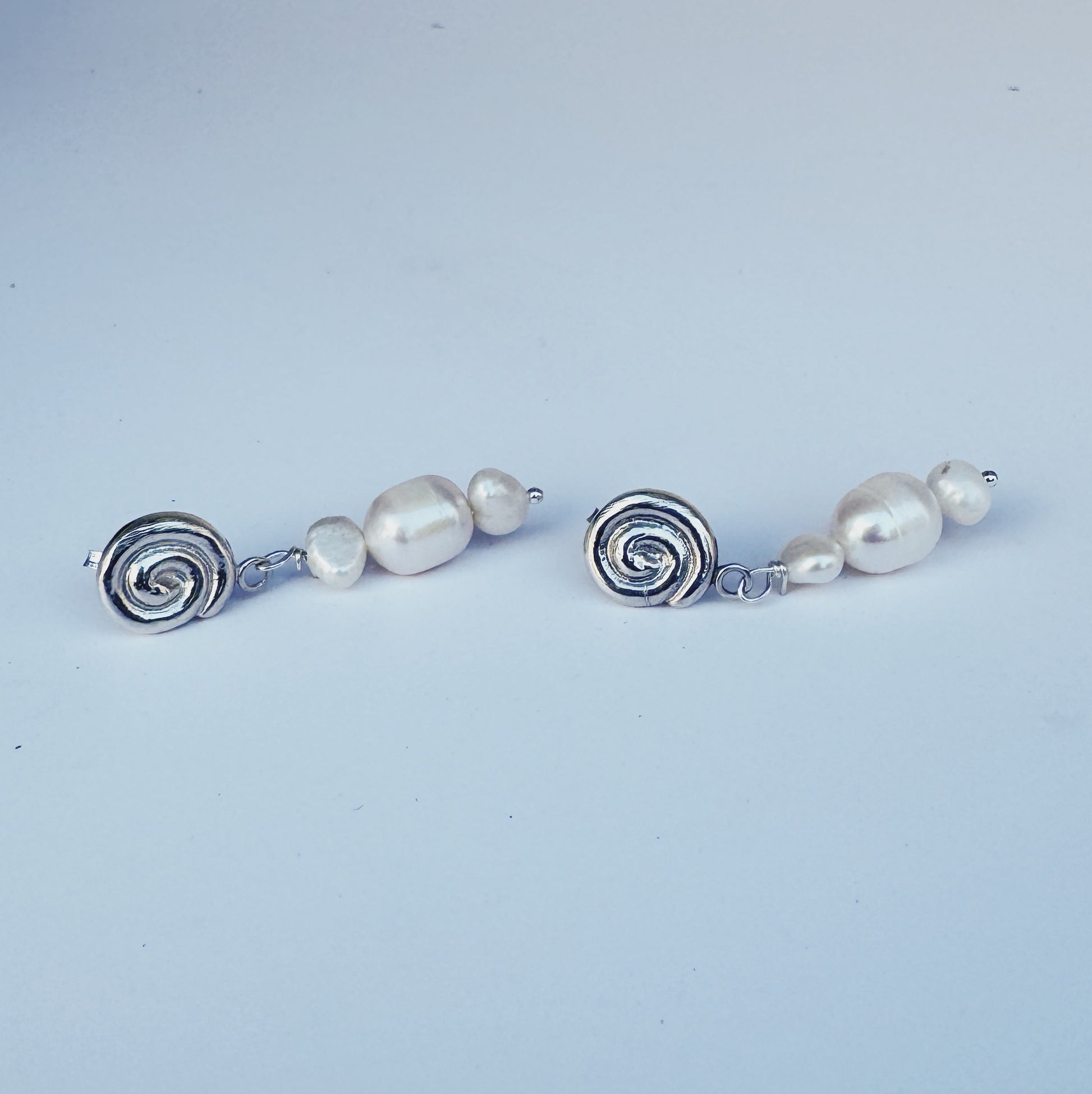 Pair of earrings with pearl beads and silver spiral designs on a light blue background