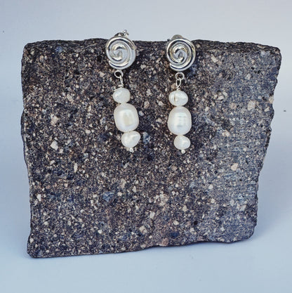 Pair of pearl earrings with silver spiral tops on a stone surface
