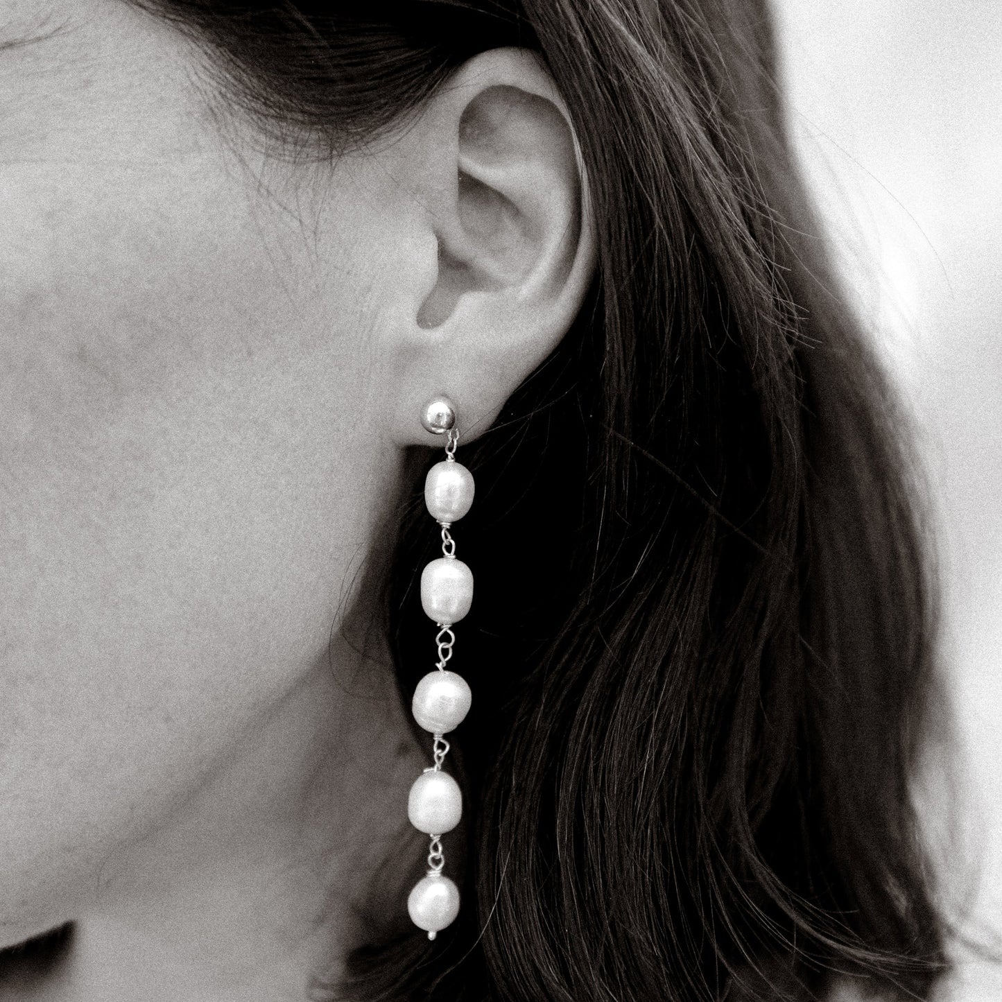 Pearl earring worn by a person with dark hair.