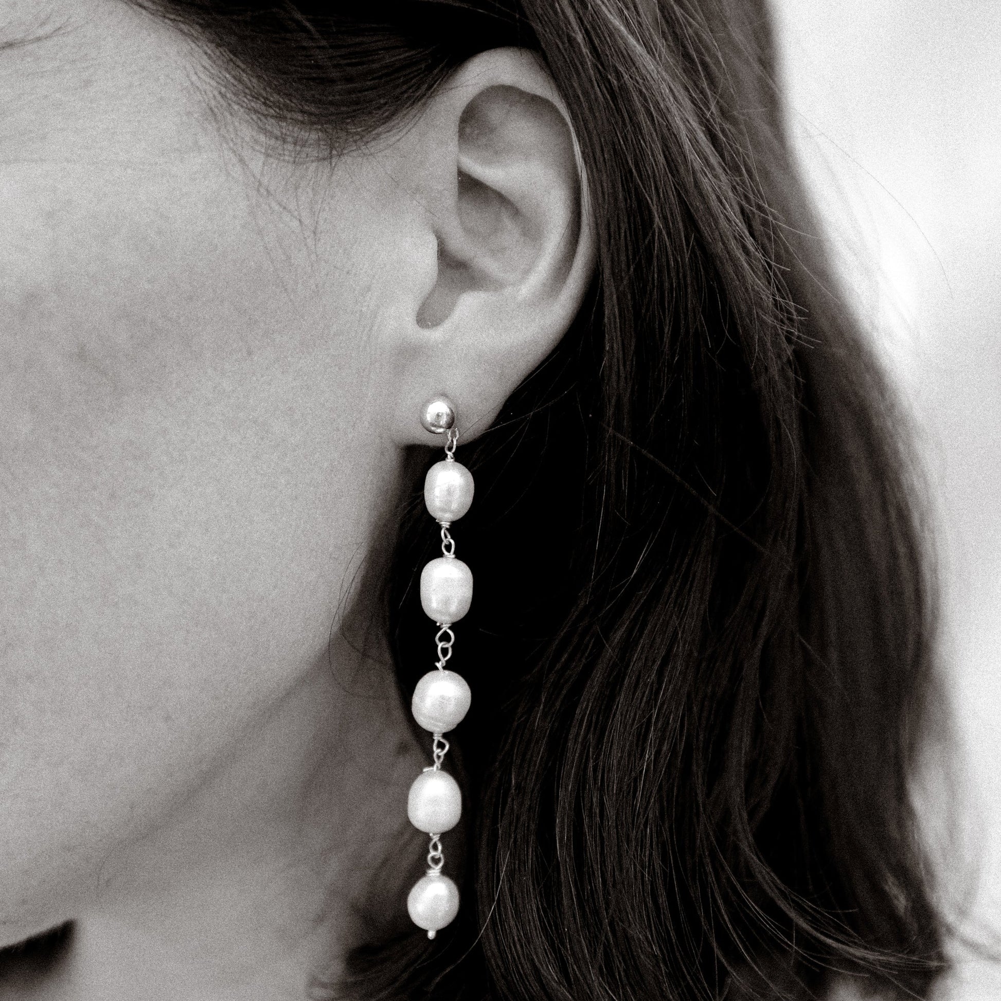 Pearl earring worn by a person with dark hair.