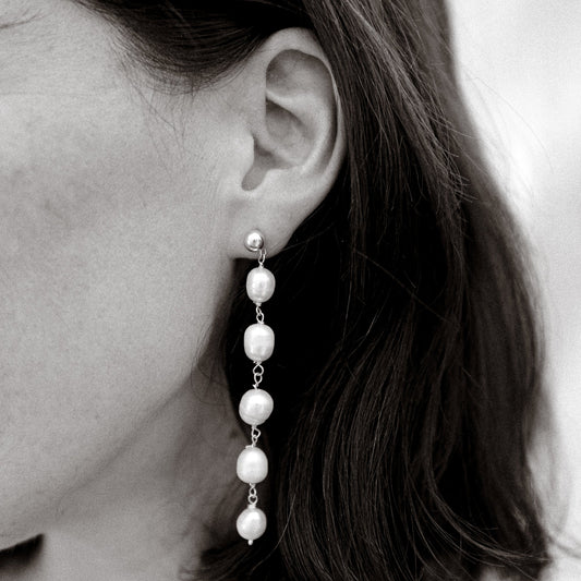 Pearl earring worn by a person with dark hair.