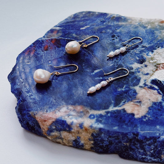 A pair of hook earrings featuring a single seed pearl on a blue stone, with gold shepherd hooks.