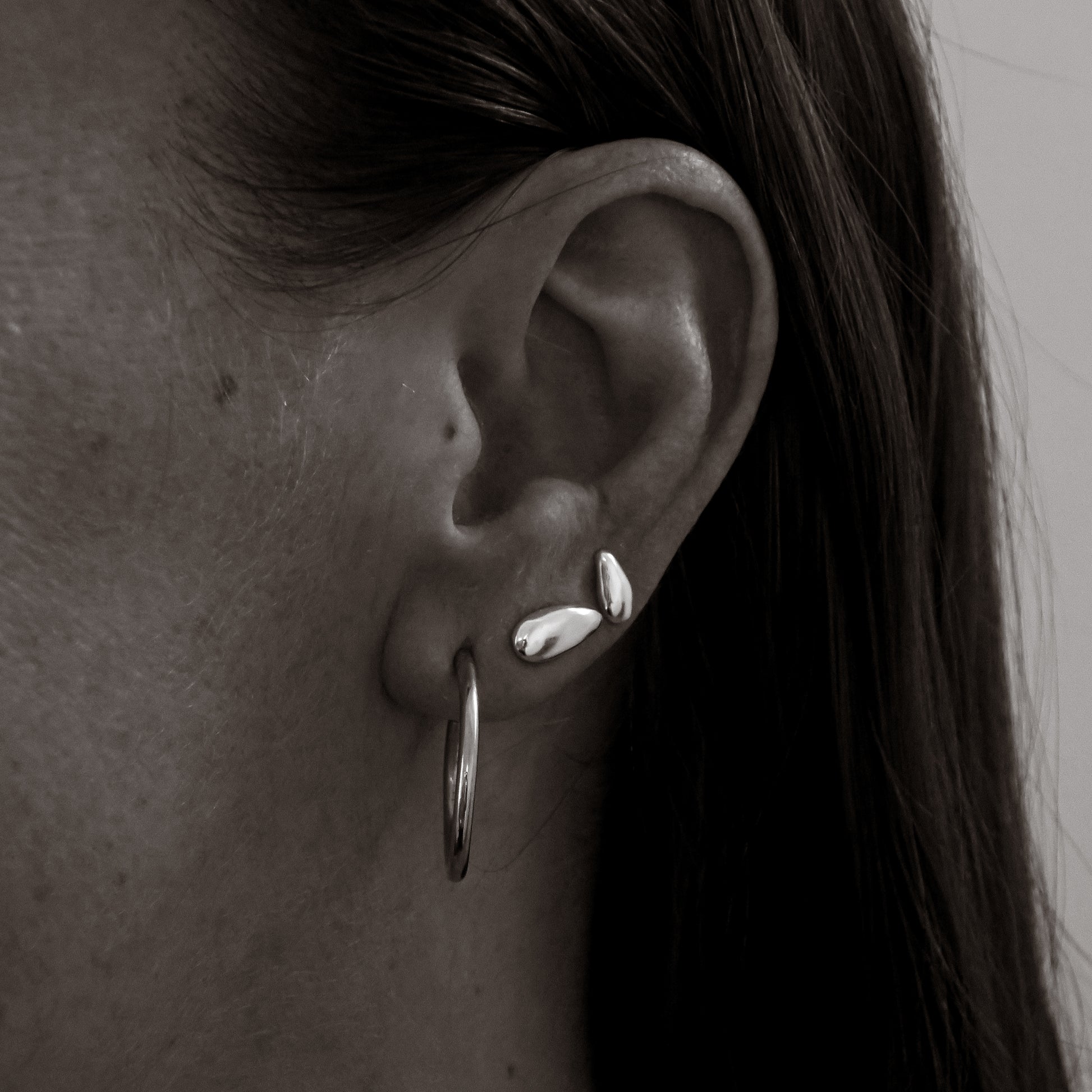 Close-up of an ear with silver hoop earrings and studs.