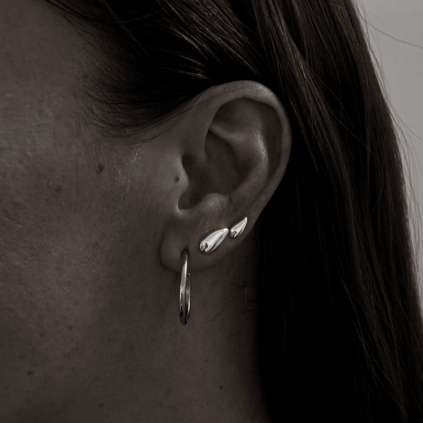 Close-up of an ear with silver earrings and hoop earring.