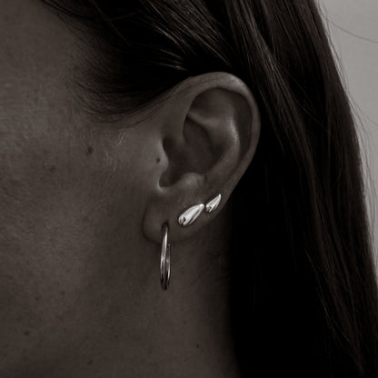 Close-up of an ear with silver earrings and hoop earring.