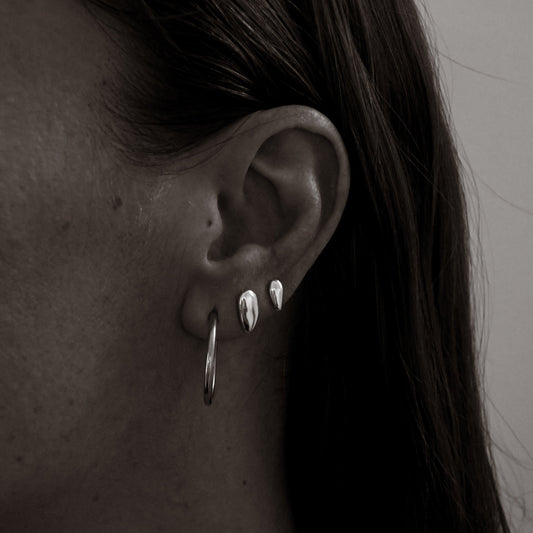 Close-up of a person wearing silver hoop earrings with a neutral background
